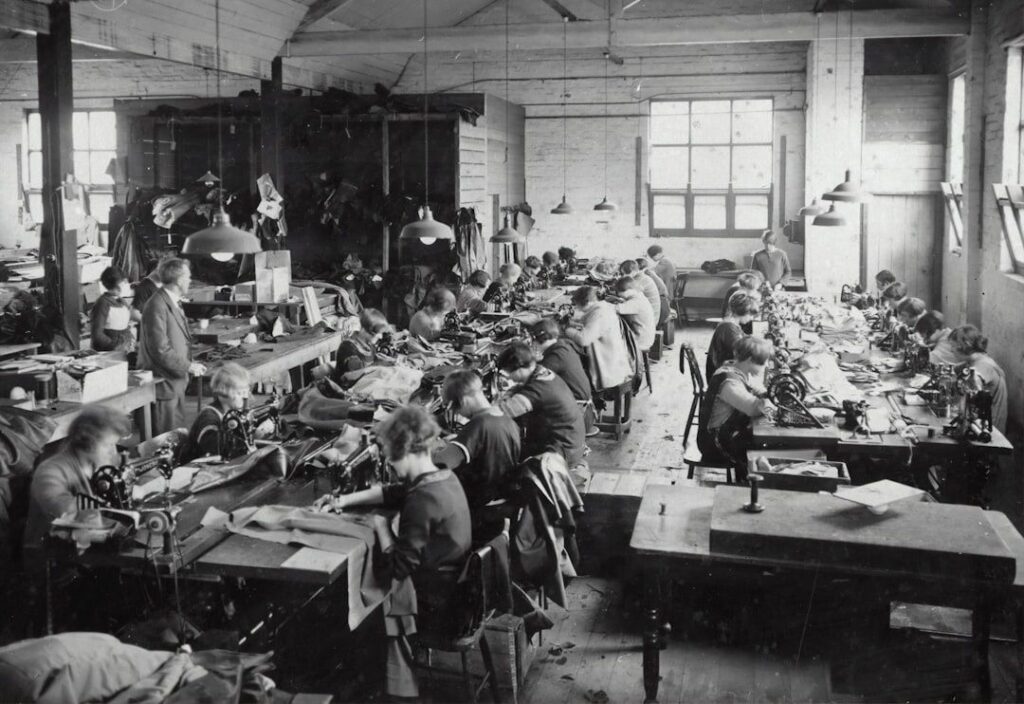 Historiskt textilverkstadsgolv med arbetare vid symaskiner
